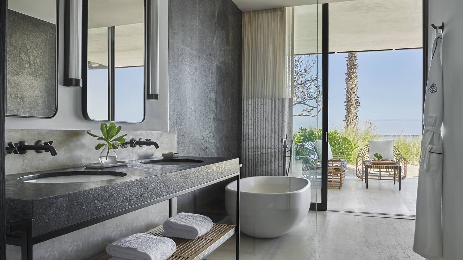 A bathroom with a large sliding glass door, bathtub, sink and towels on a shelf.