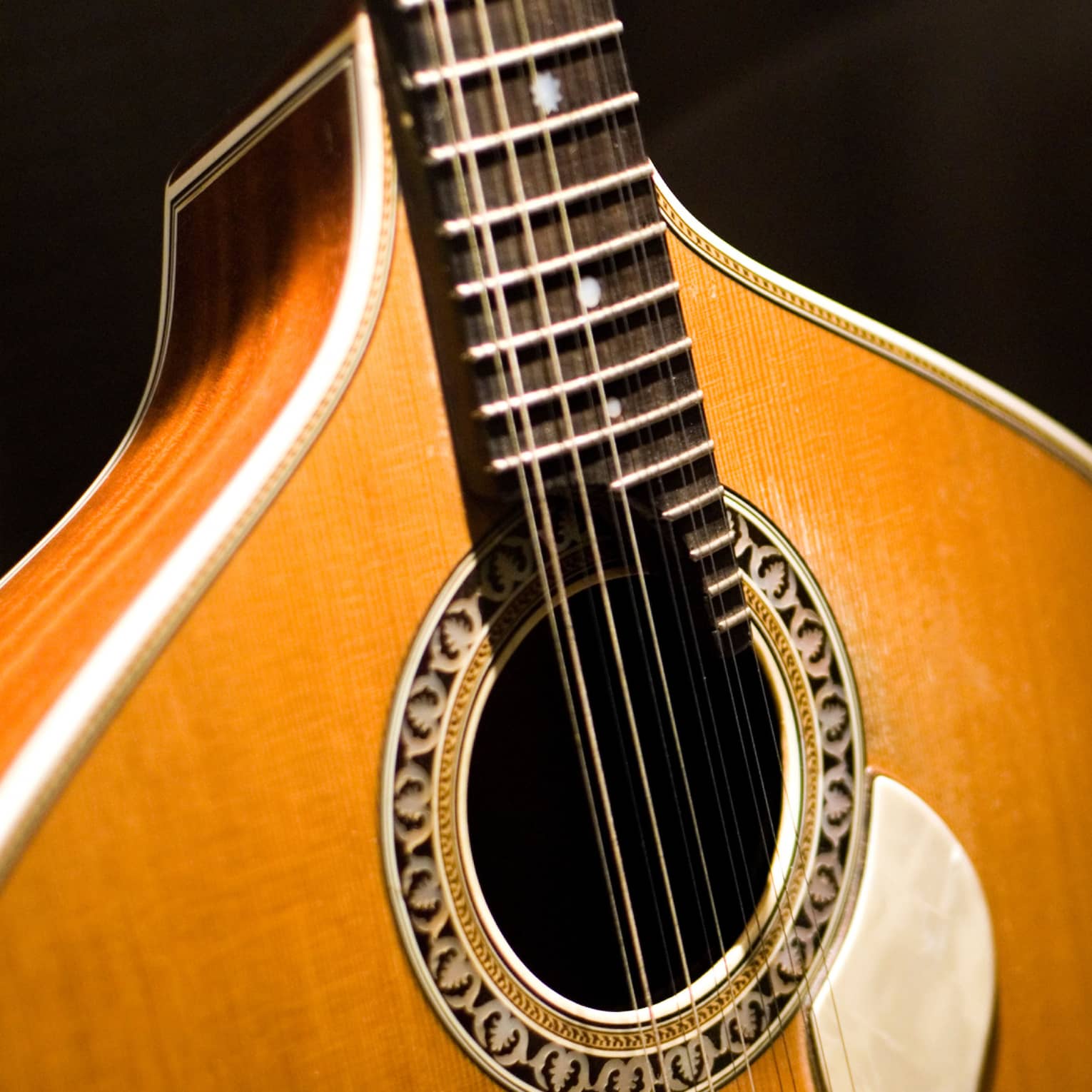Close-up of a 12-string Fado guitar: inlaid rosette around the sound hole, pear-shaped top connecting to the fretboard.