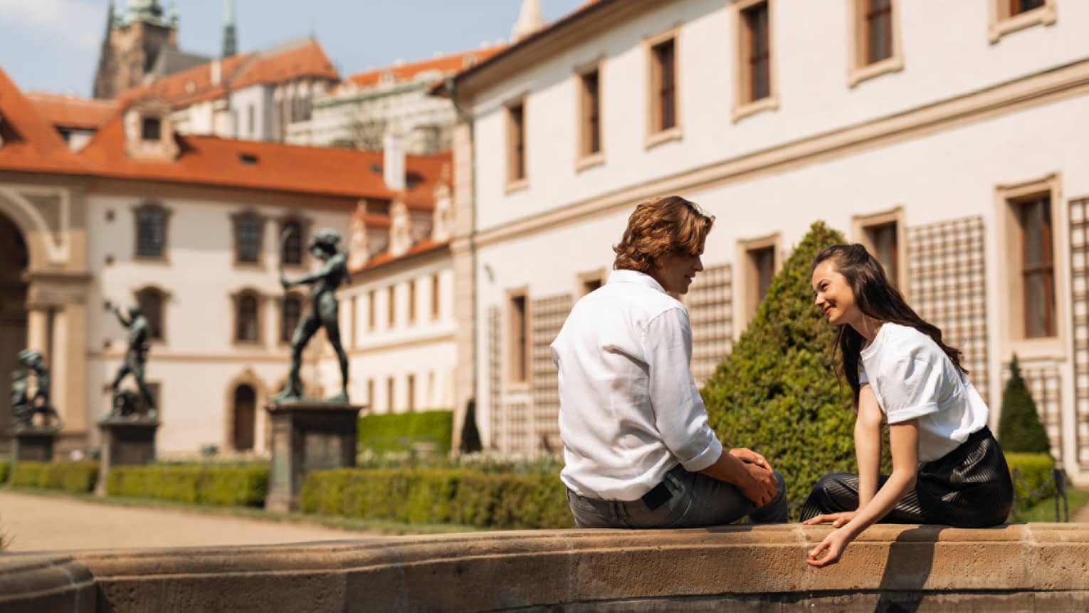Couple seated on low courtyard wall beside Prague Castle