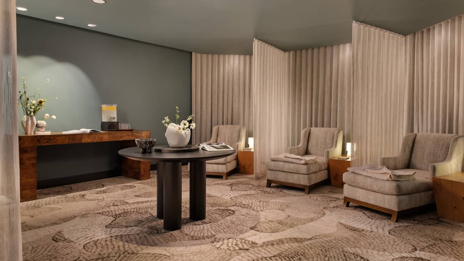 Spa relaxation area with tan armchairs separated by curtains, round table in middle of room with vase of flowers