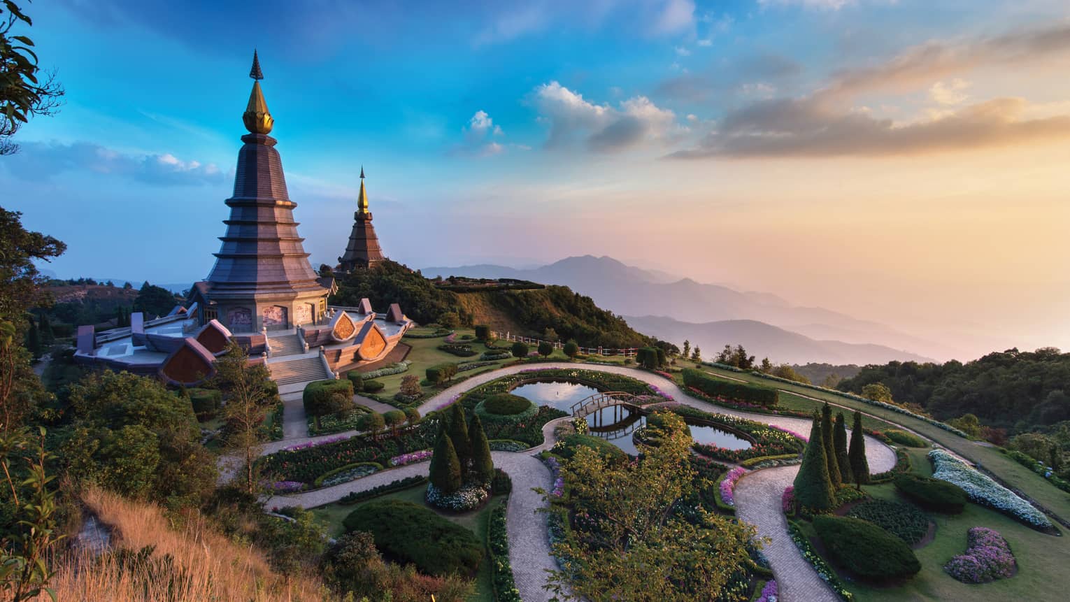 Majestic twin pagodas surrounded by lush gardens and winding paths, set against a backdrop of misty mountains at sunset.