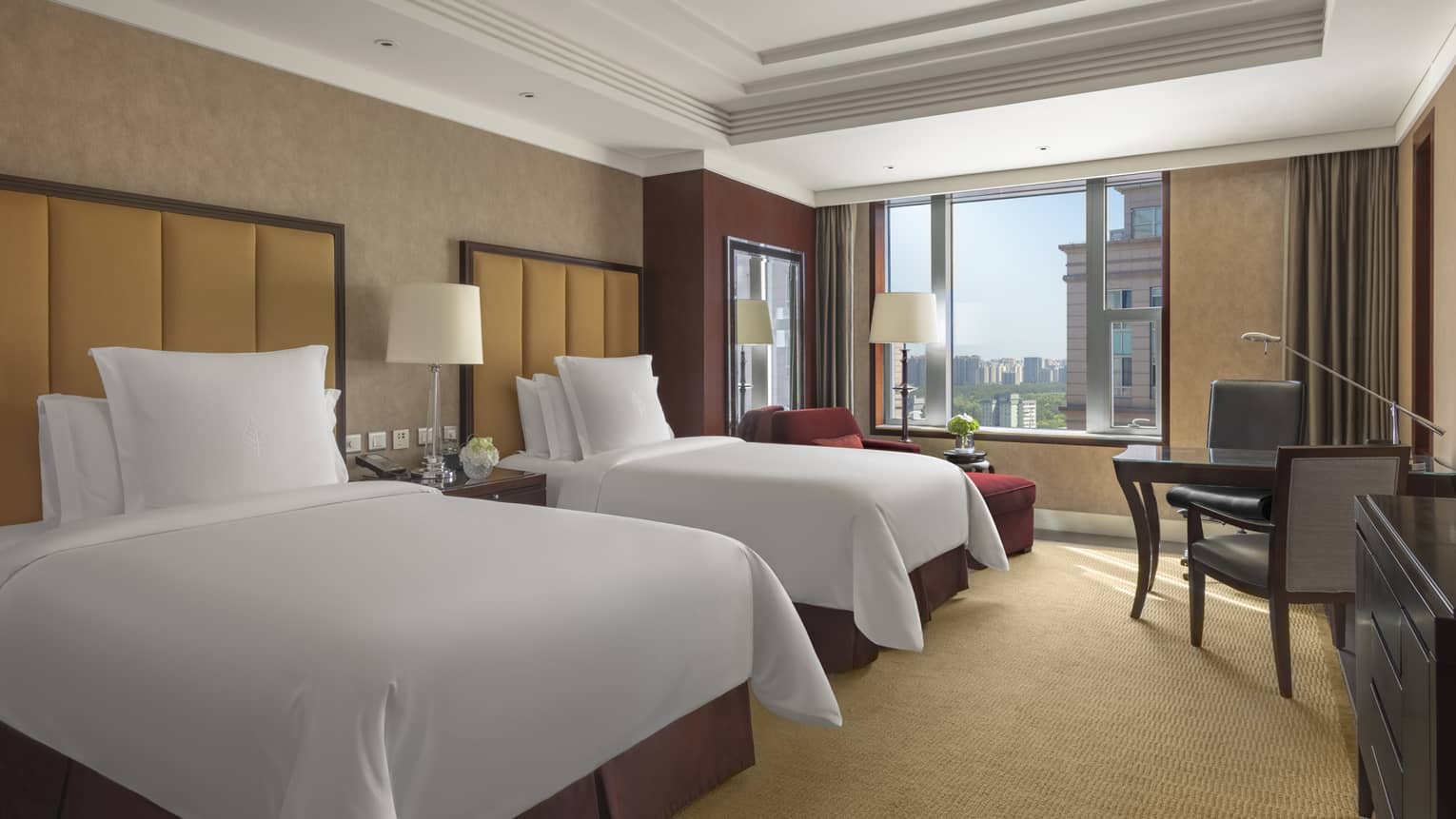 Hotel room with two single beds, light brown walls, tan carpet, table with two chairs and window