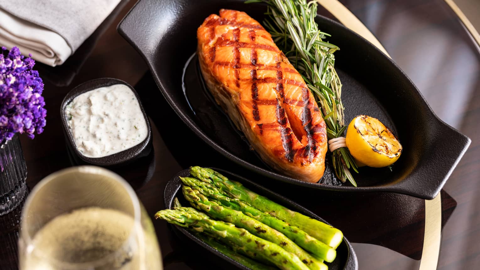 Seared salmon steak in cast iron dish with herb and lemon garnish and a side of grilled asparagus