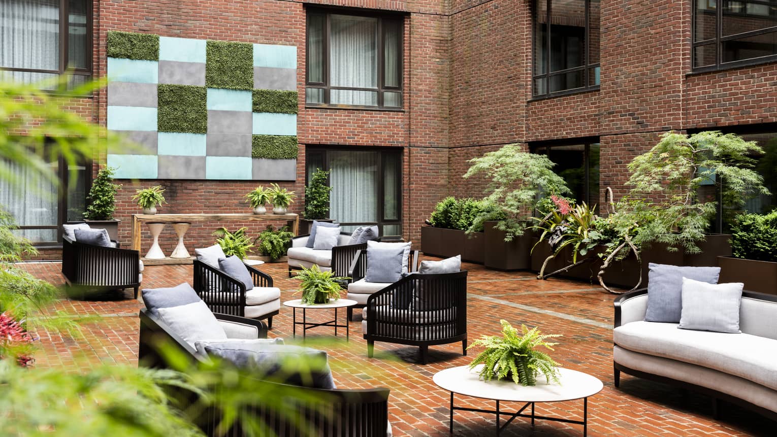 An outdoor seating area with grey sofas and chairs, surrounded by red brick walls.