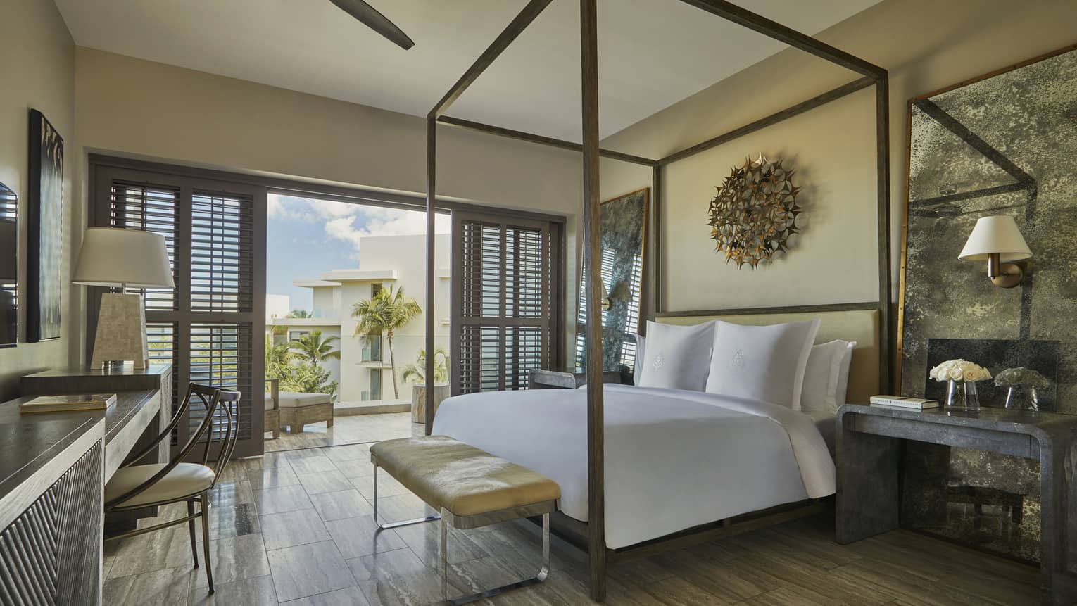 Resort View Room with canopy bed, small brown leather bench, desk, patio doors with wood shutters
