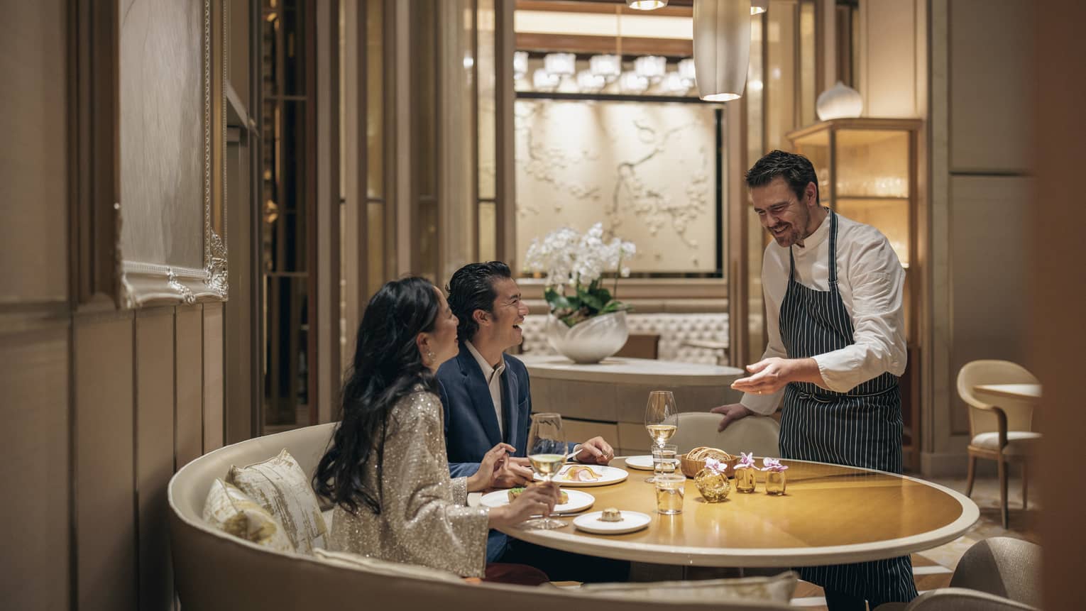 Couple dines at circular table at est, sommelier presenting them with a bottle of wine