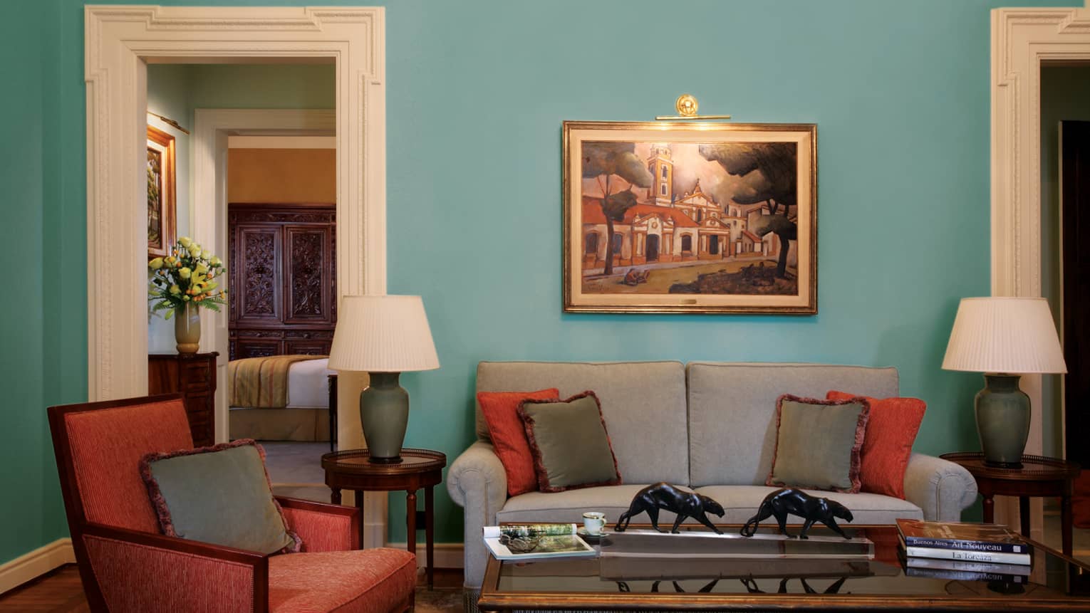 La Mansión Royale Suite living room with teal walls, grey sofa and red armchair