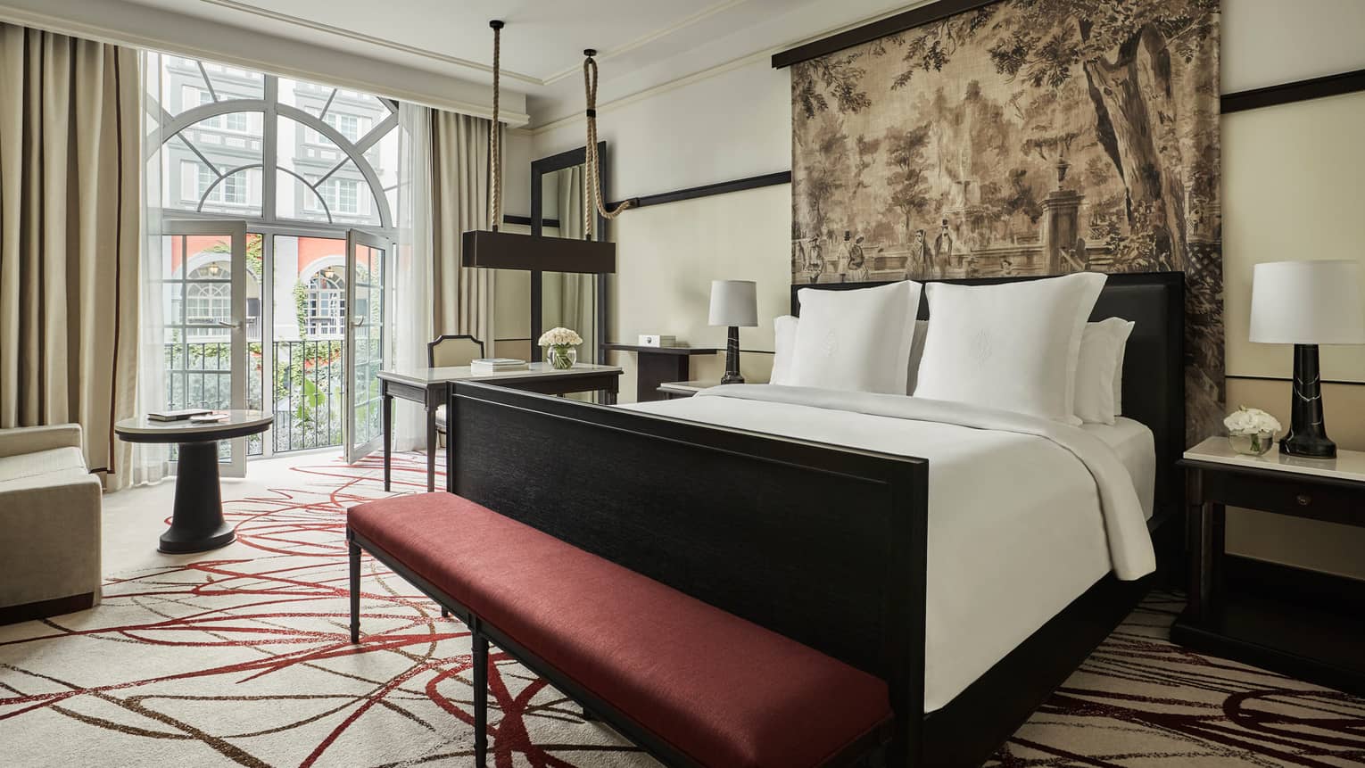 Premier Room bed under print headboard, red bench at foot, sunny arched balcony glass doors