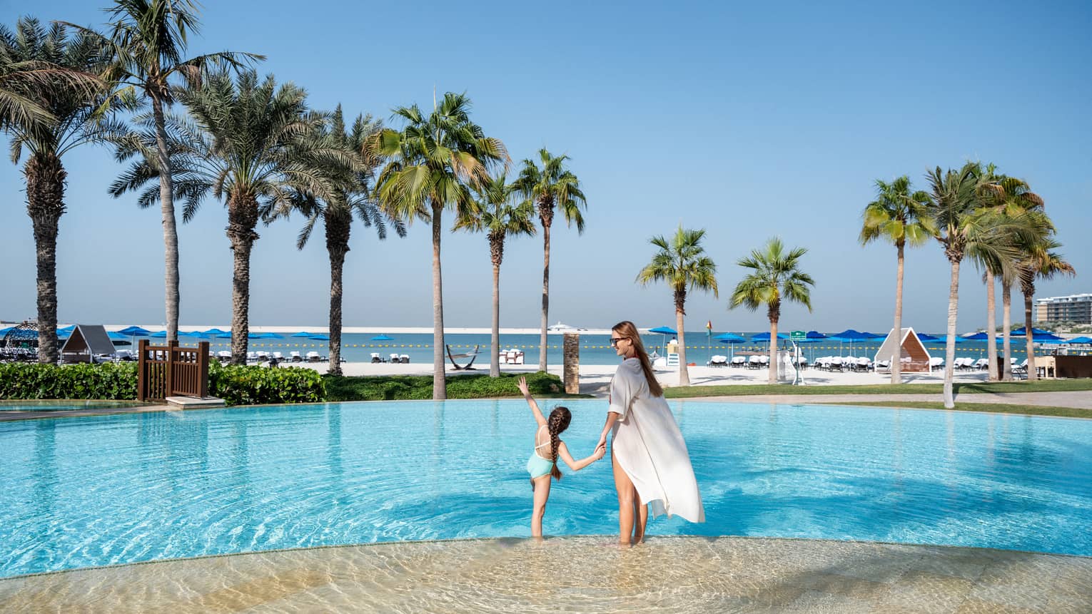 A woman and a little girl hold hands while wading in the outdoor pool overlooking the Arabian Gulf