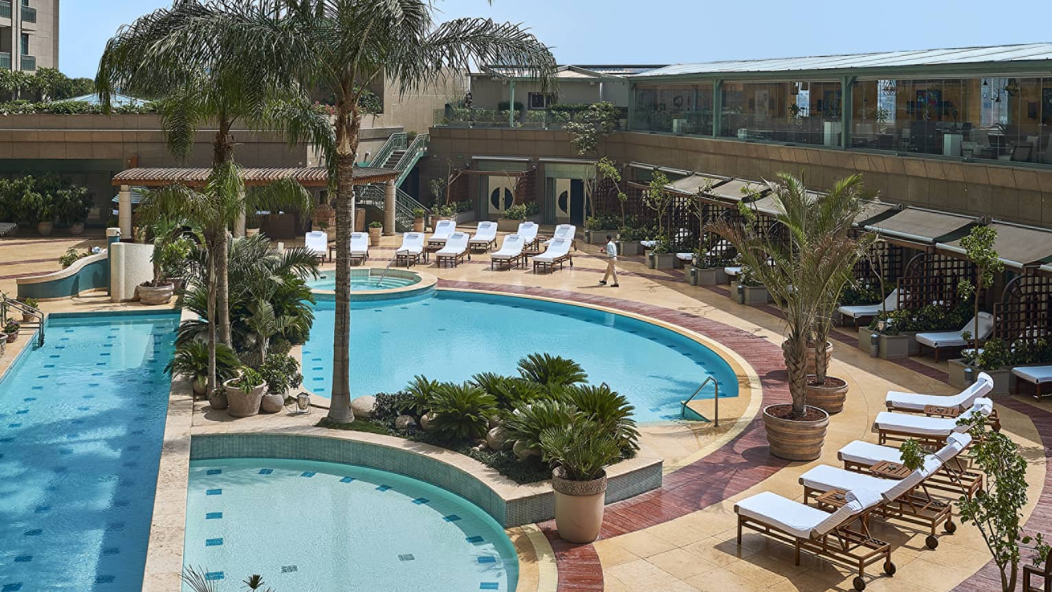 Aerial view of three swimming pools lined with palms, lounge chairs and row of cabanas