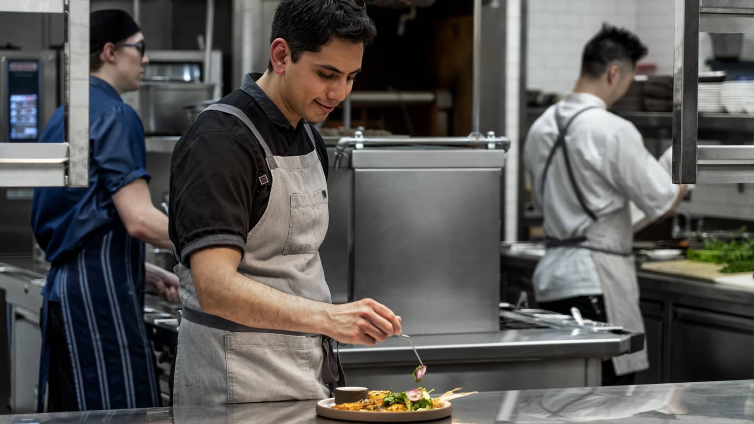 Restaurant chef places radish on salad at steel counter on kitchen line