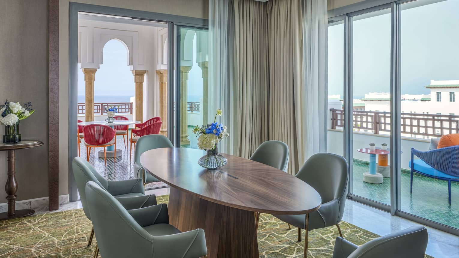 Luxury hotel suite at Four Seasons Hotel Rabat, featuring an oval, wooden dining table with 6 turquoise-coloured chairs and a large terrace