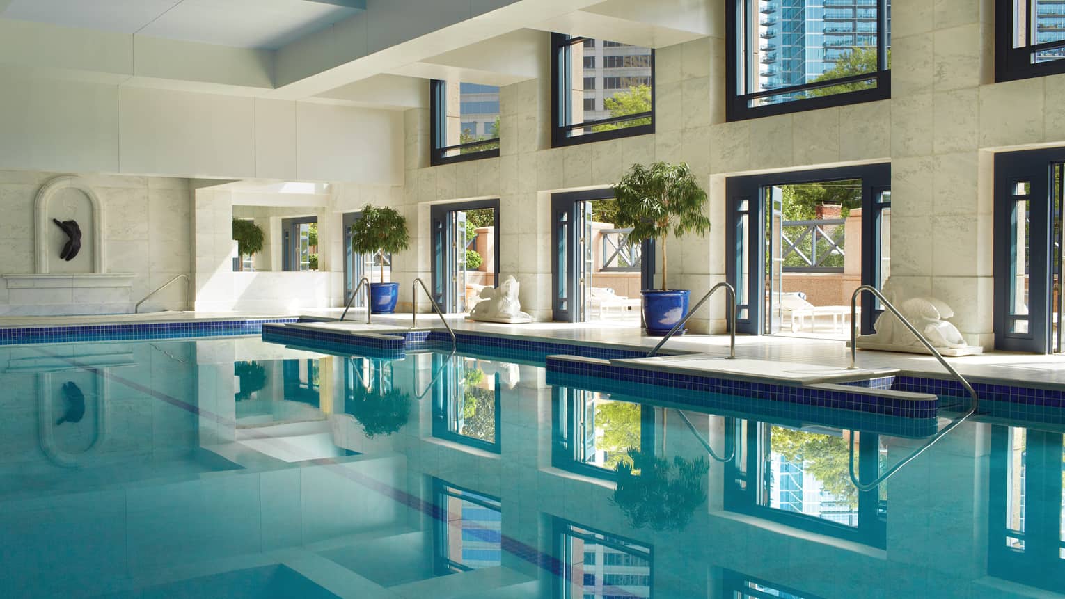 Saltwater lap swimming pool under white marble walls, tall sunny windows