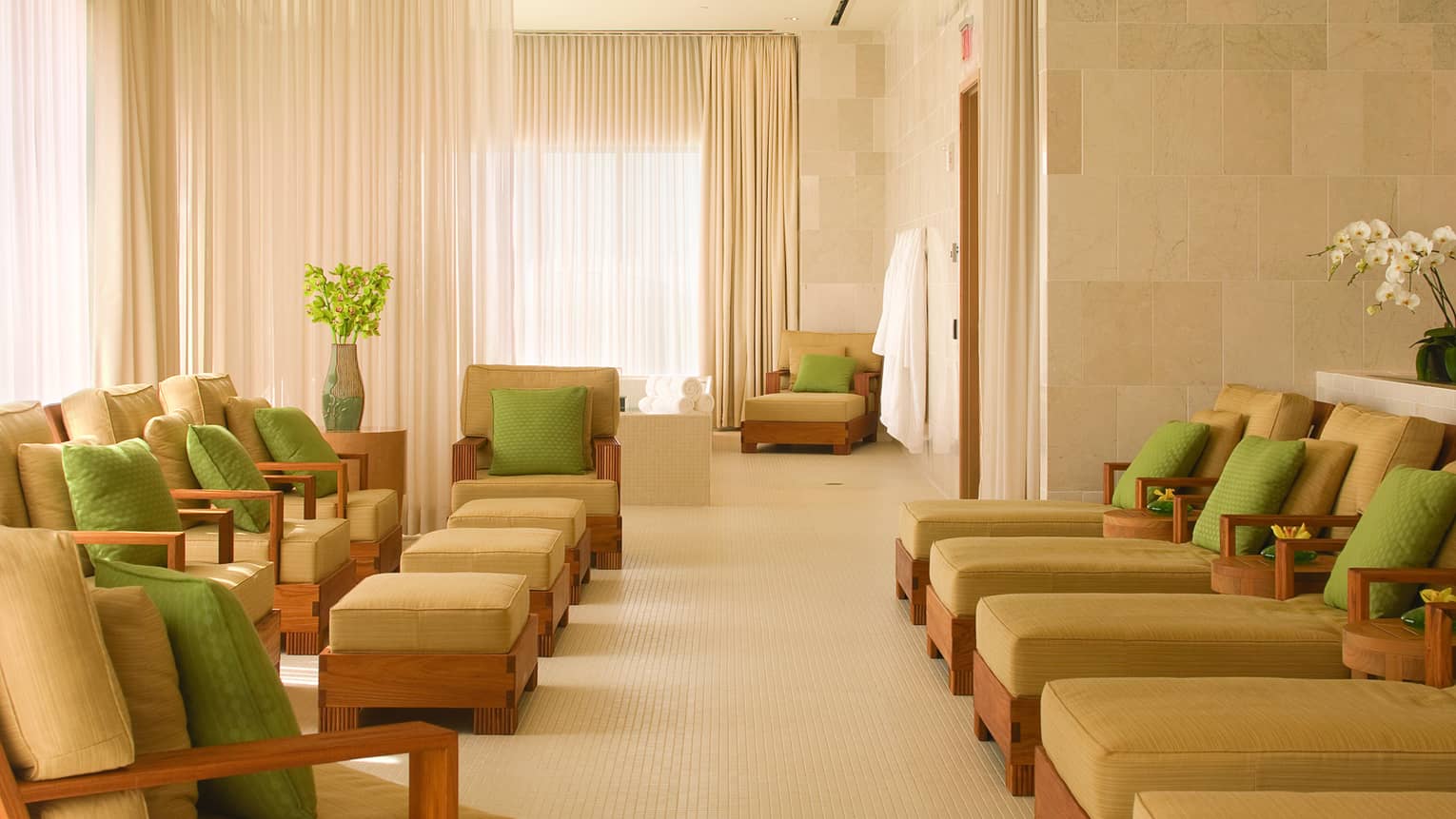 Spa lounge with rows of plush beige chairs and chaise lounges with lime green accent pillows
