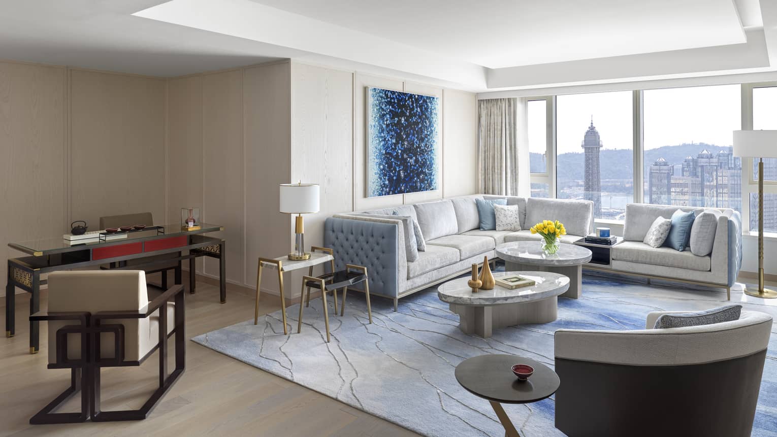 Imperial Suite with white leather sectional, marble nesting tables, dining table, accent chair, blue decor, floor-to-ceiling window with city views