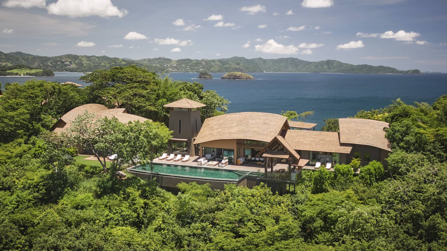 A luxurious oceanfront villa surrounded by lush greenery, with a private infinity pool and panoramic views of the ocean and nearby islands.