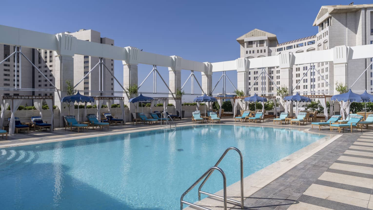 Outdoor pool surrounded by teal lounge chairs and white column