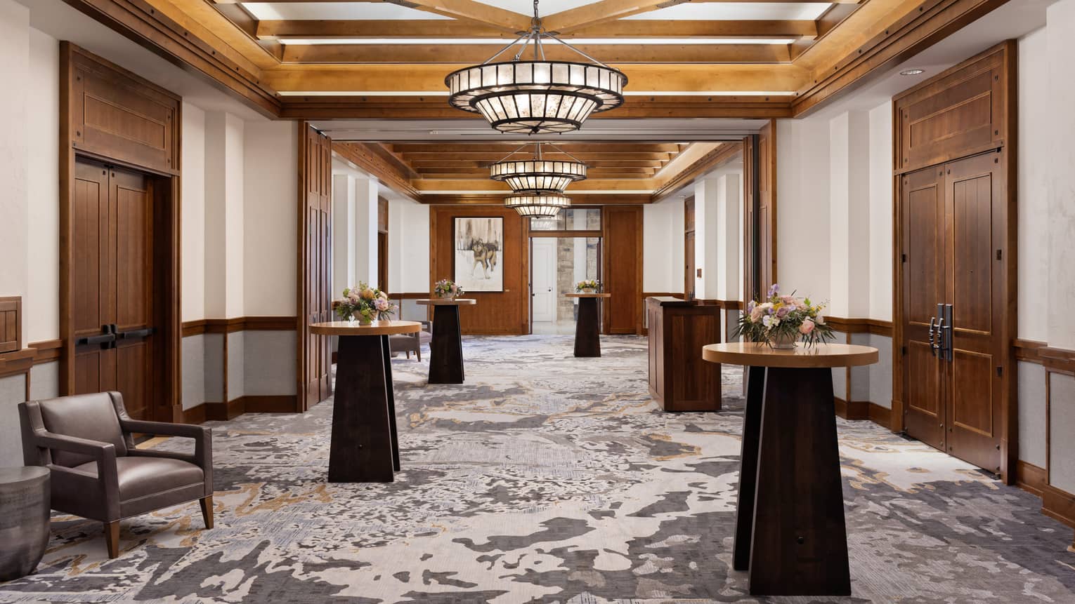 A foyer with standing tables, a large chandelier and large wooden doors.
