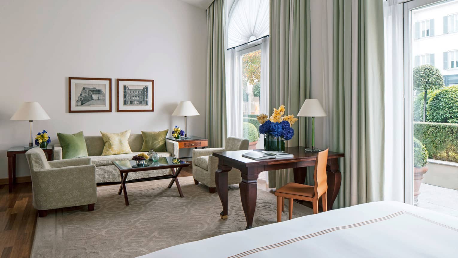 Junior Suite sofa, chairs, wood desk with flowers by two tall sunny windows