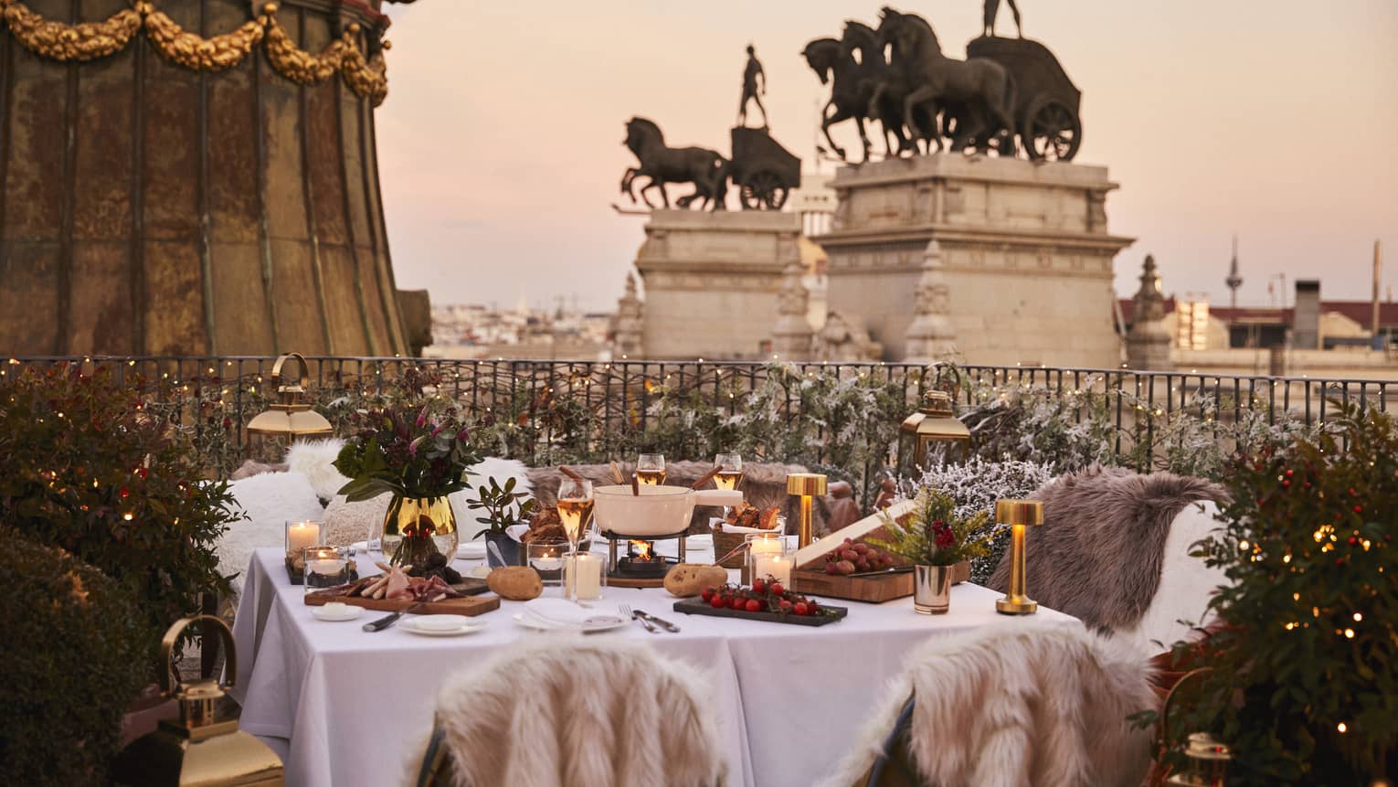 Terrace with table set with winter d�cor and fur throws, overlooking tall statues at dusk