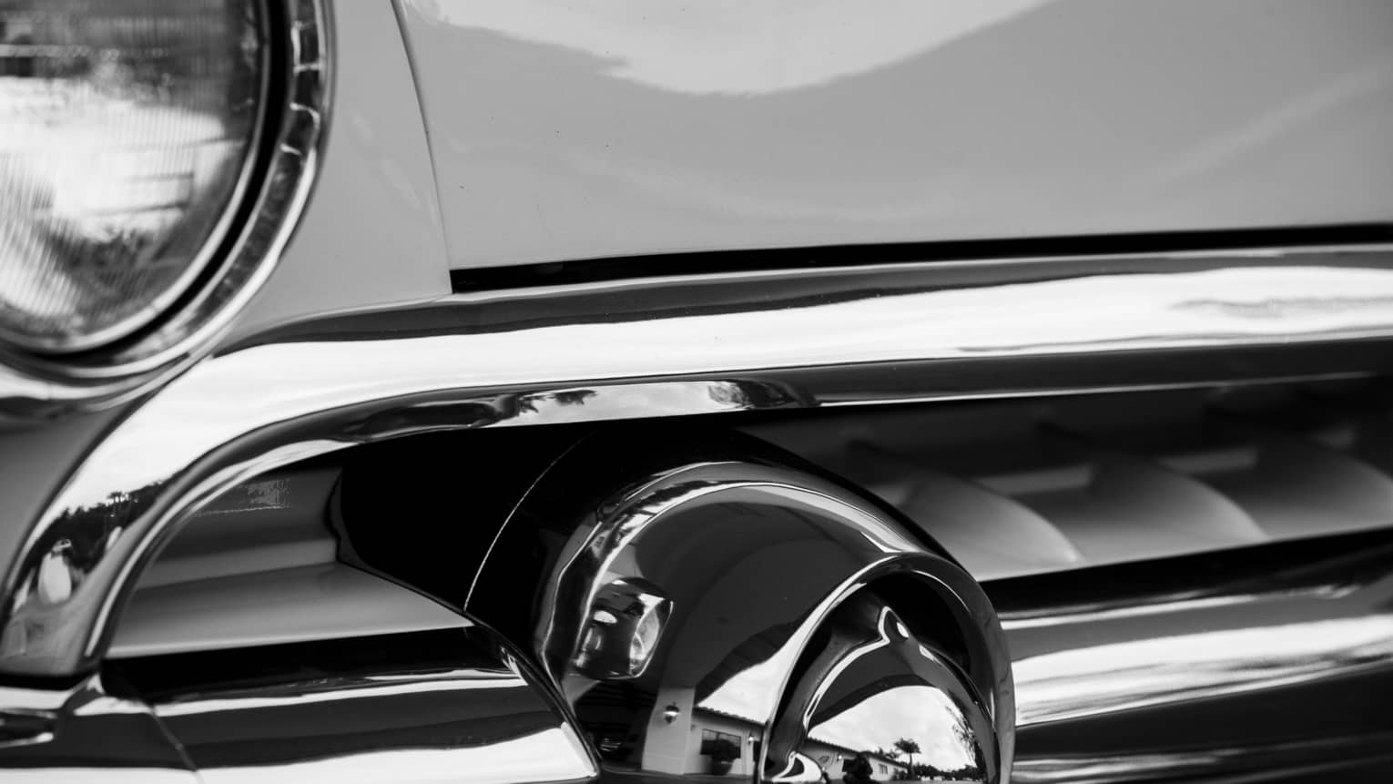 Black and white photo close-up of luxury car shiny metal grill, headlight 