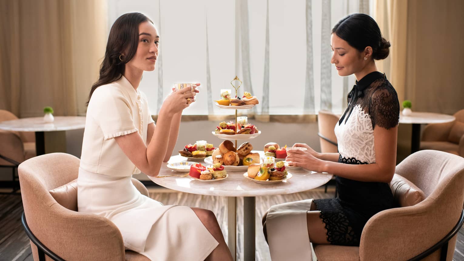 Two guests enjoy a formal tea service including sumptuous sweets and pastries and a three-tiered stand laden with delicacies.