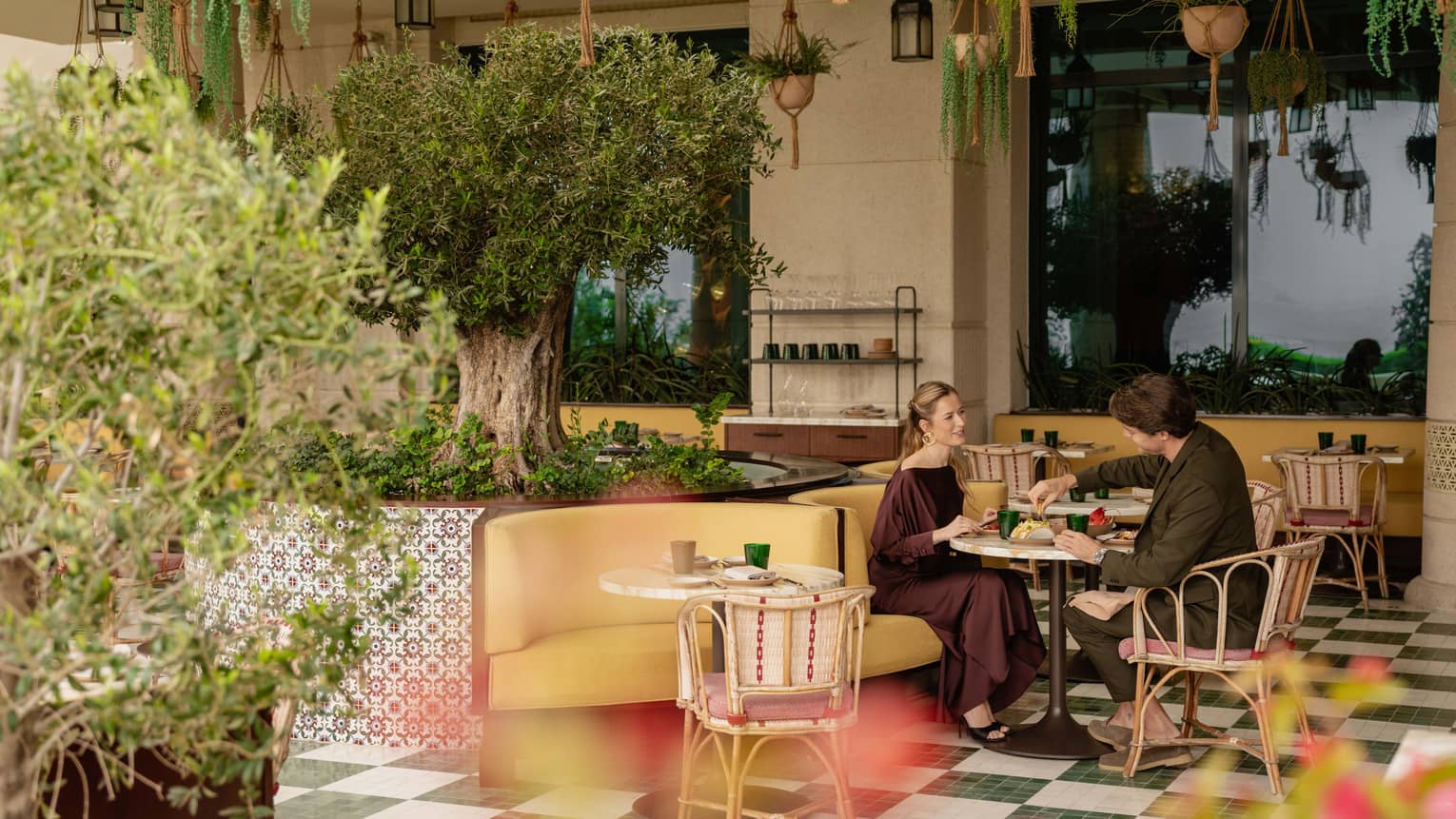 A couple dines at a colourful outdoor patio with green, checkered floors, mosaic tiles and lush greenery