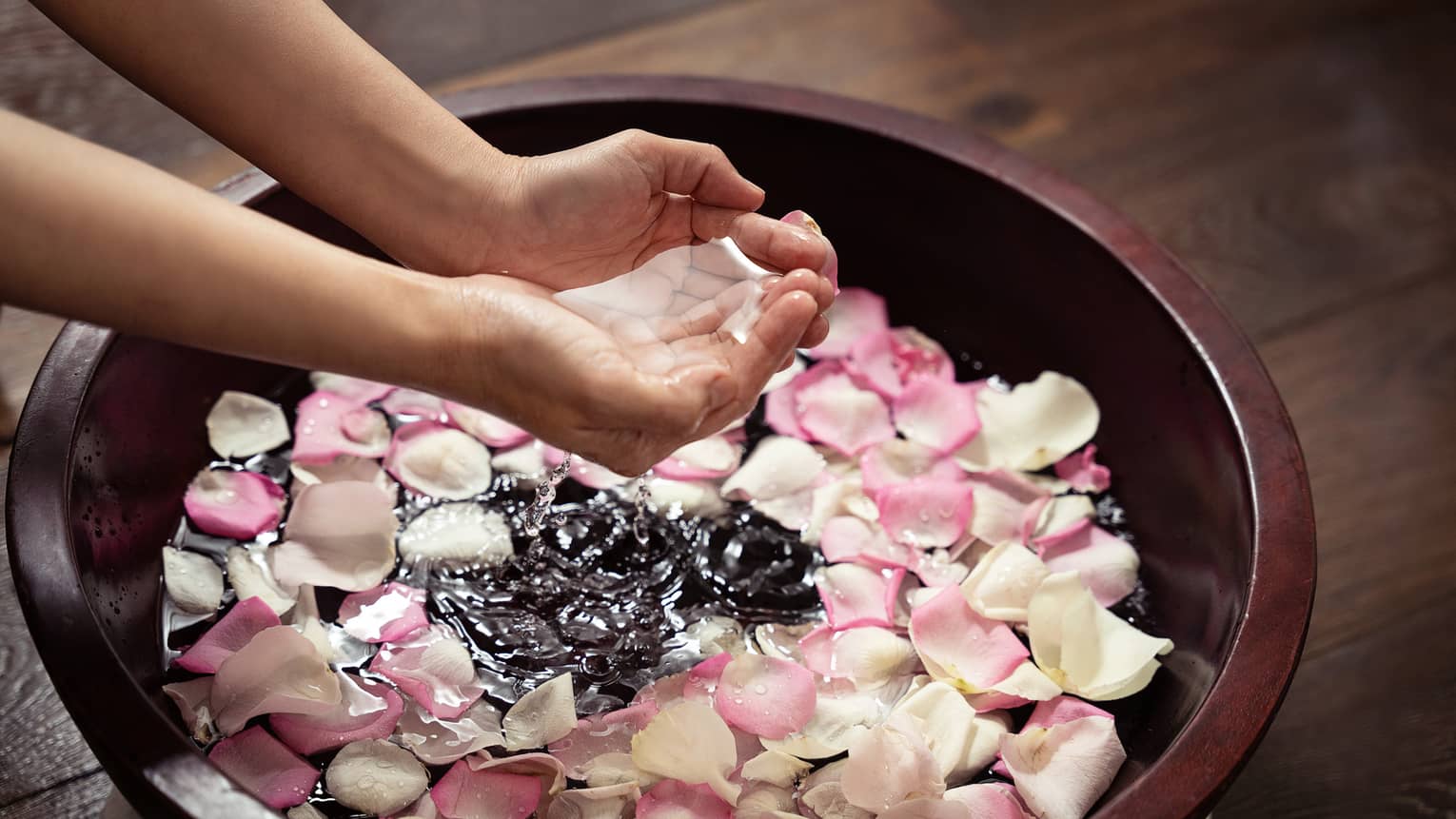 Pari fo hands clasped together brings water up from a large bowl filled with pink and white rose petals