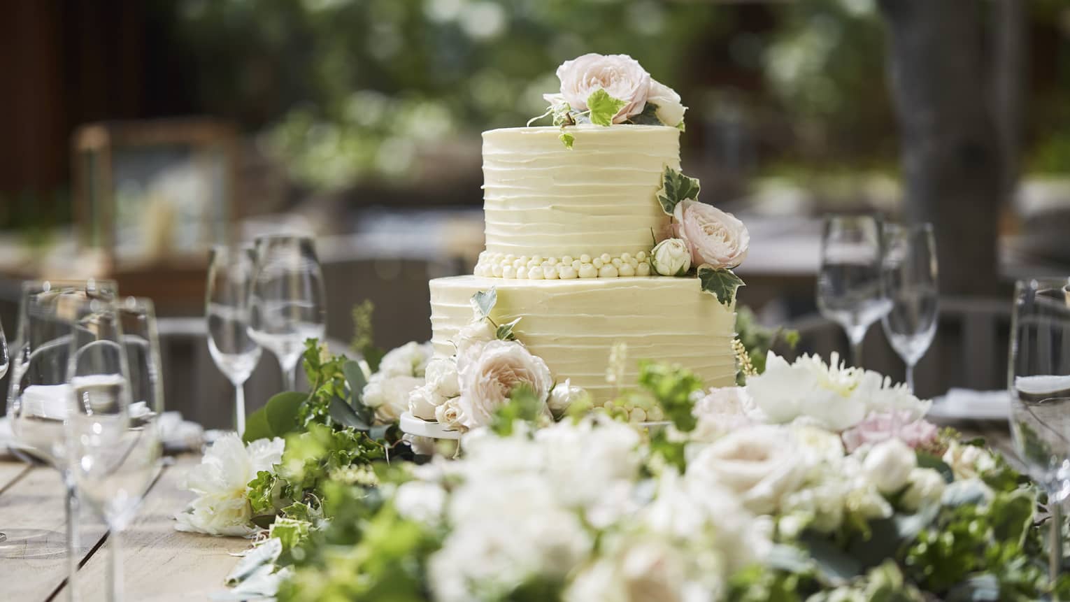 Two-tiered white wedding cake on banquet table with wine glasses, flowers