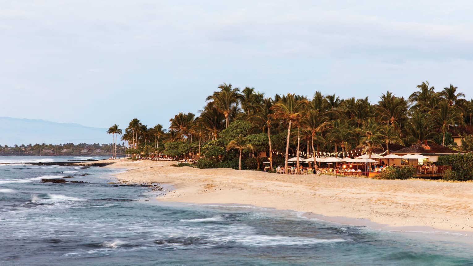 View over ocean and white sand beach to event on resort lawn