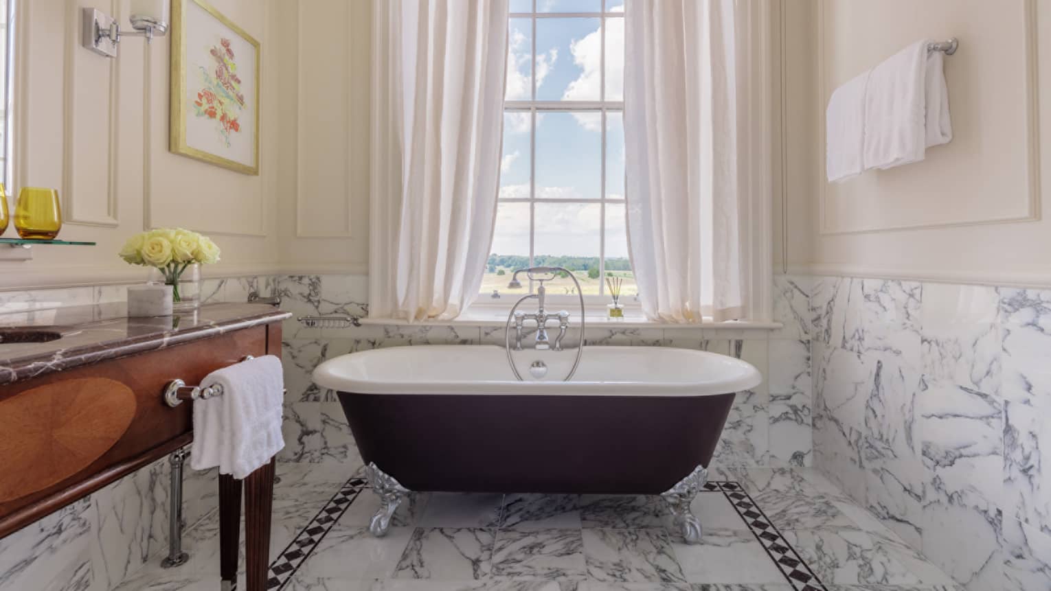Bathroom with marble accents, large clawfoot tub, wooden vanity, window with white drapes