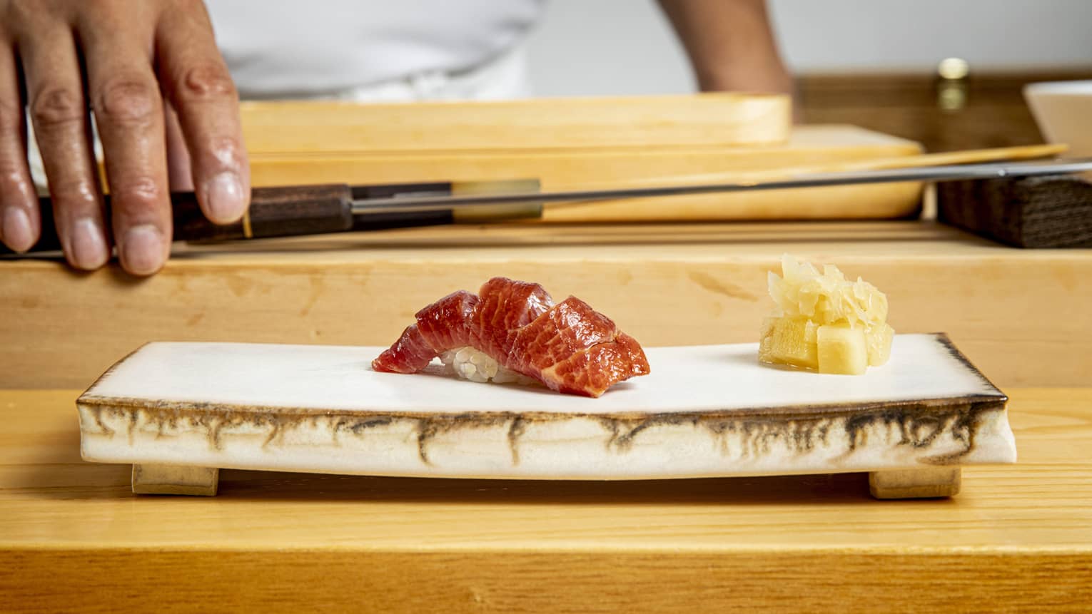 Edomae sushi on a modern stone plate, with a chef and chef's knife in the background