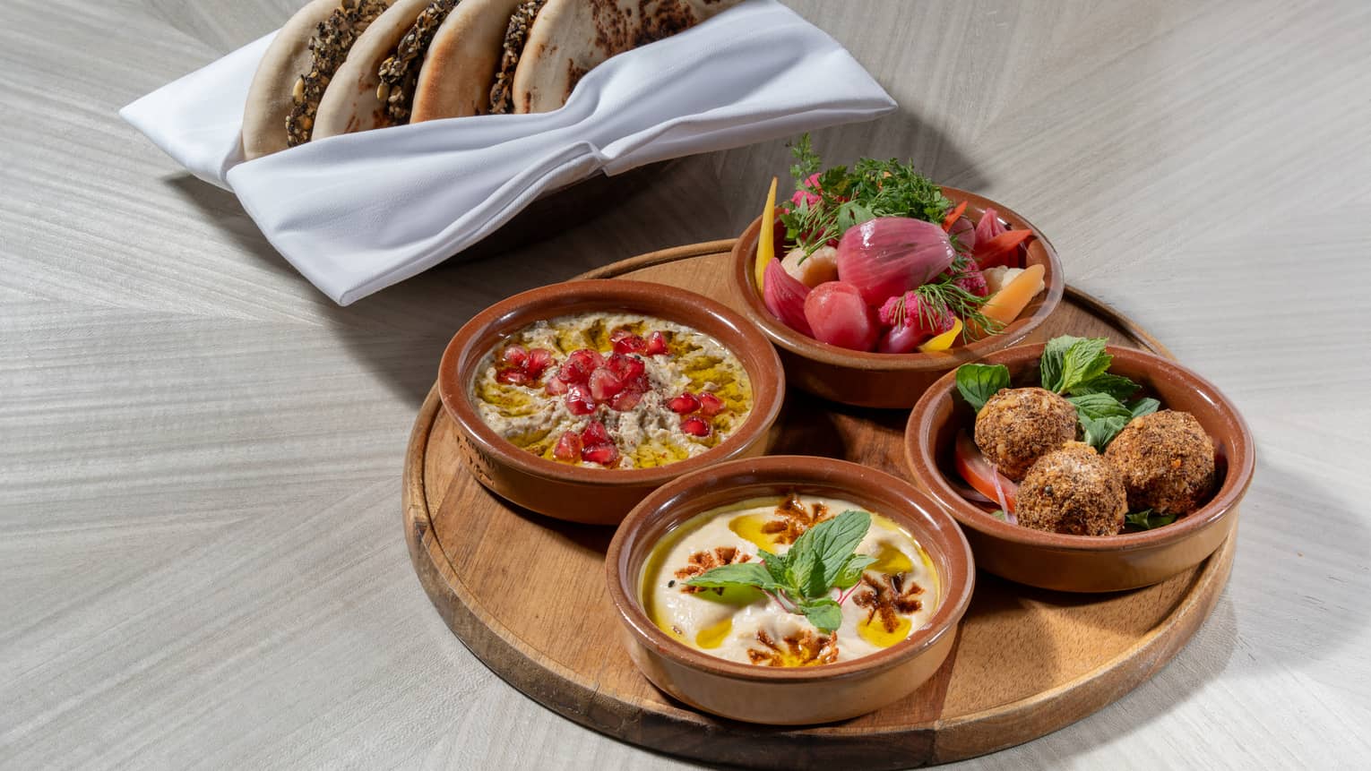 Platter topped with four small bowls of mezze with a basket of naan on the side