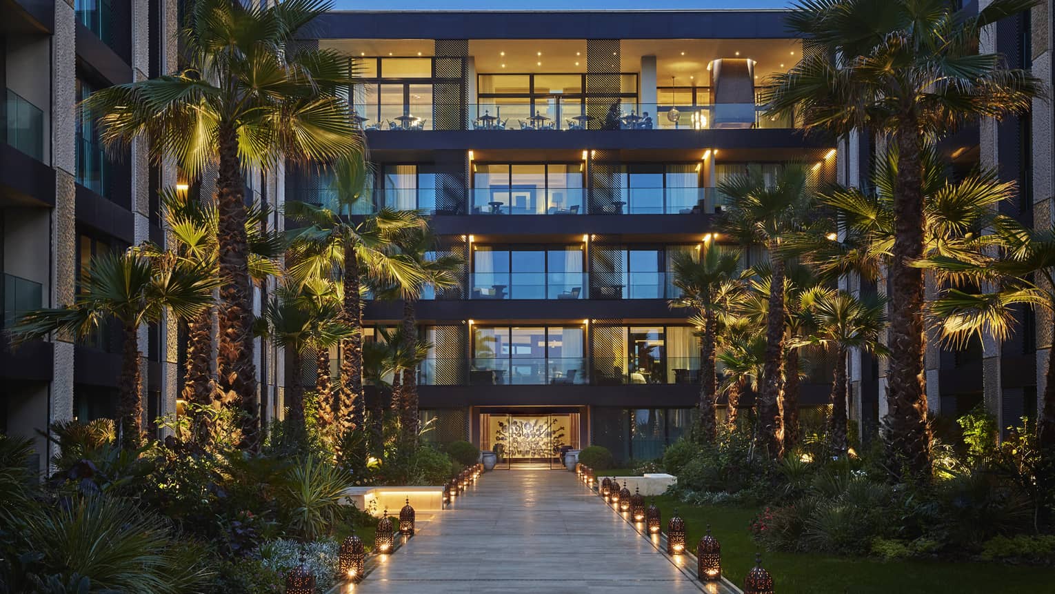 Lanterns. palm trees with lights along walkway under Four Seasons Hotel Casablanca building at dusk