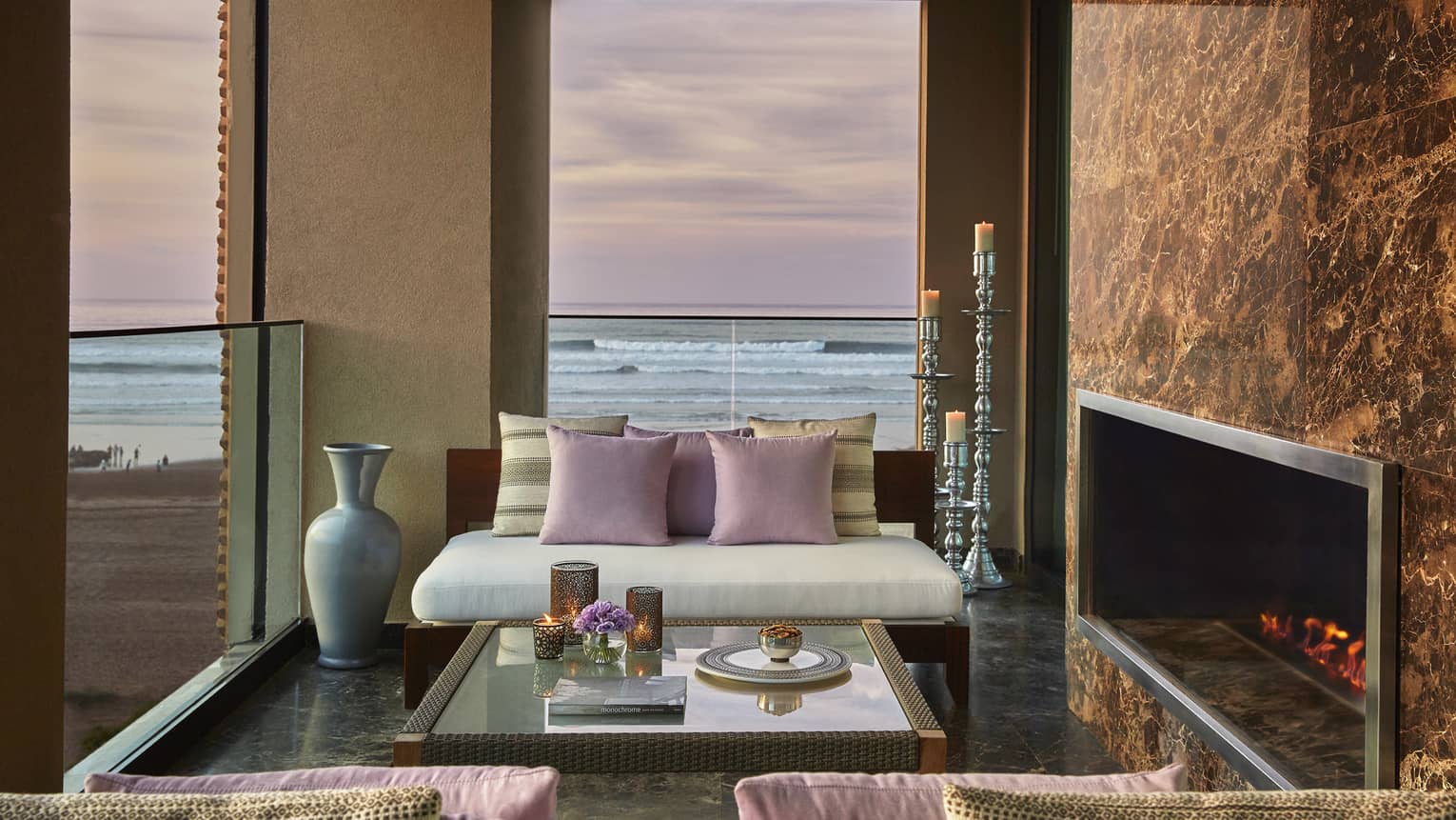Royal Suite Ocean View white sofa, pink pillows by fireplace, under window with pink sunset, ocean