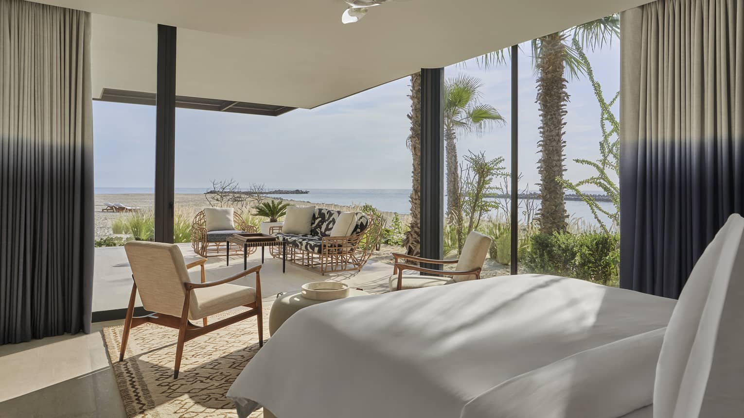 Two Bedroom Sunrise Suite with King bed, white linens, twin armchairs, floor-to-ceiling window with ocean views