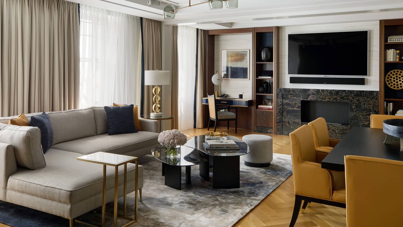 L-shaped grey sofa by coffee table, large TV over fireplace, dining chairs