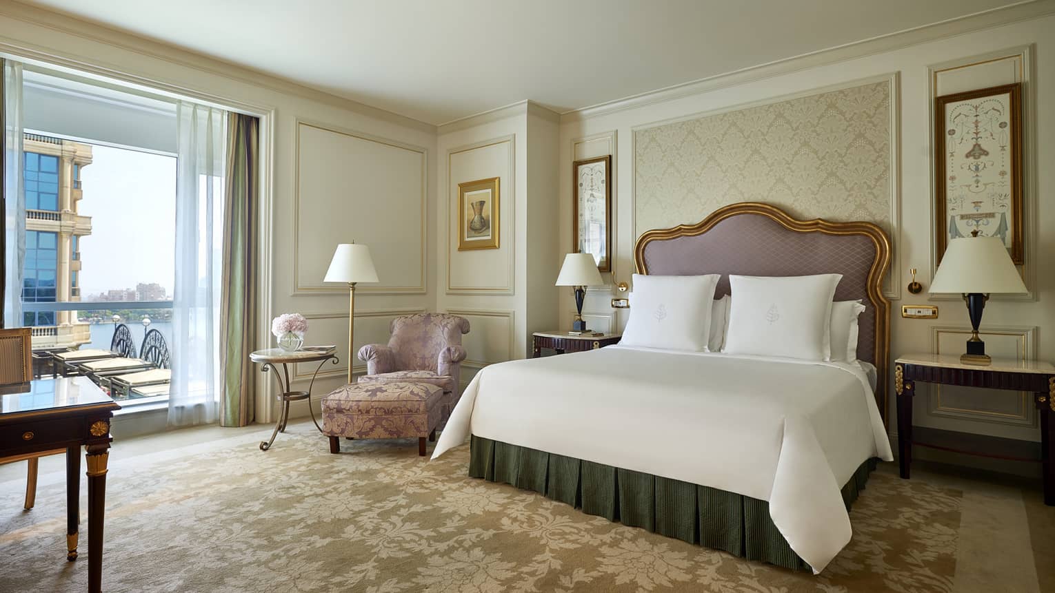 Superior Room bed with padded headboard with gold trim, pink satin armchair by patio door
