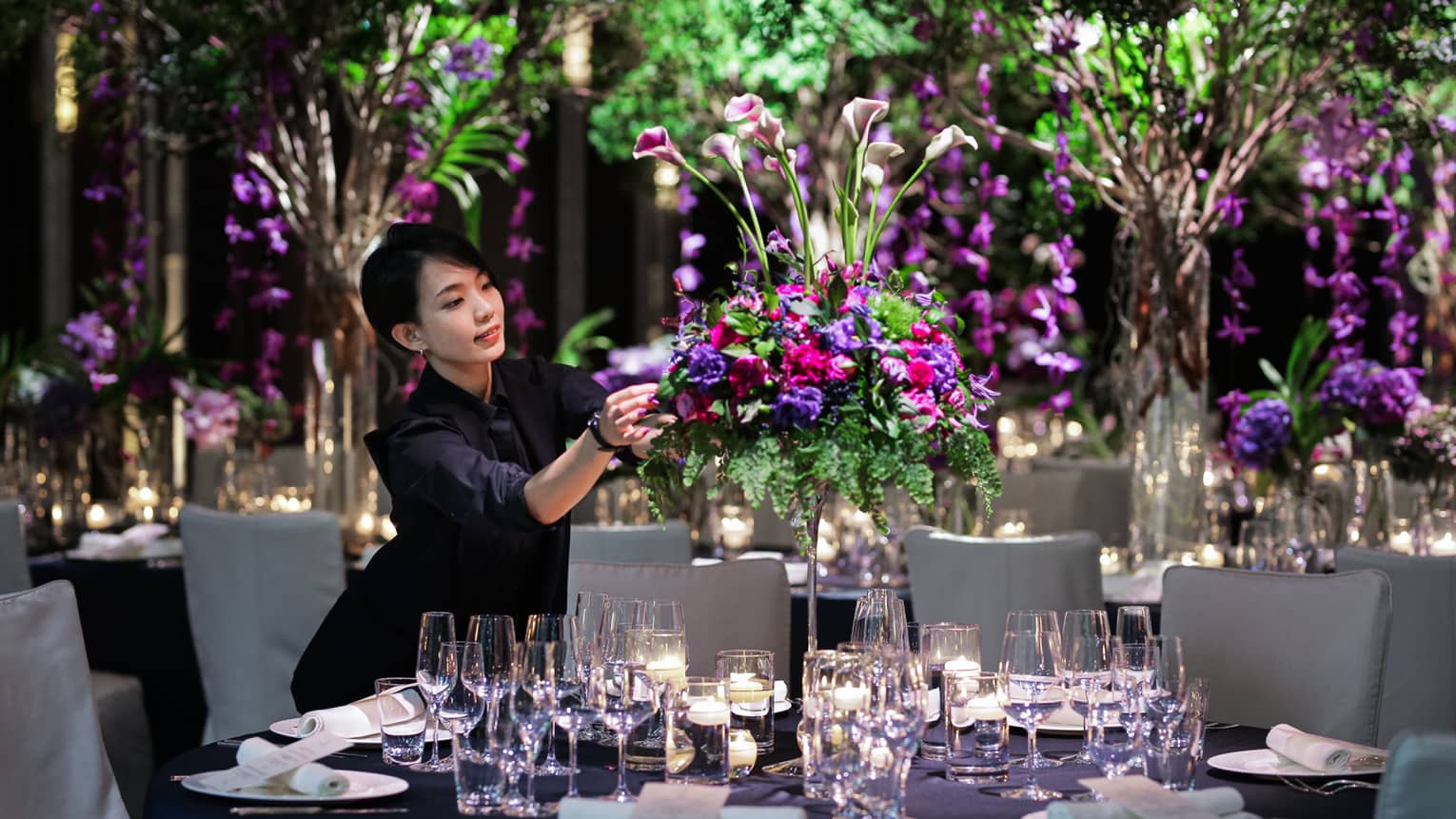 Wedding event staff arranges large floral centrepiece on banquet table