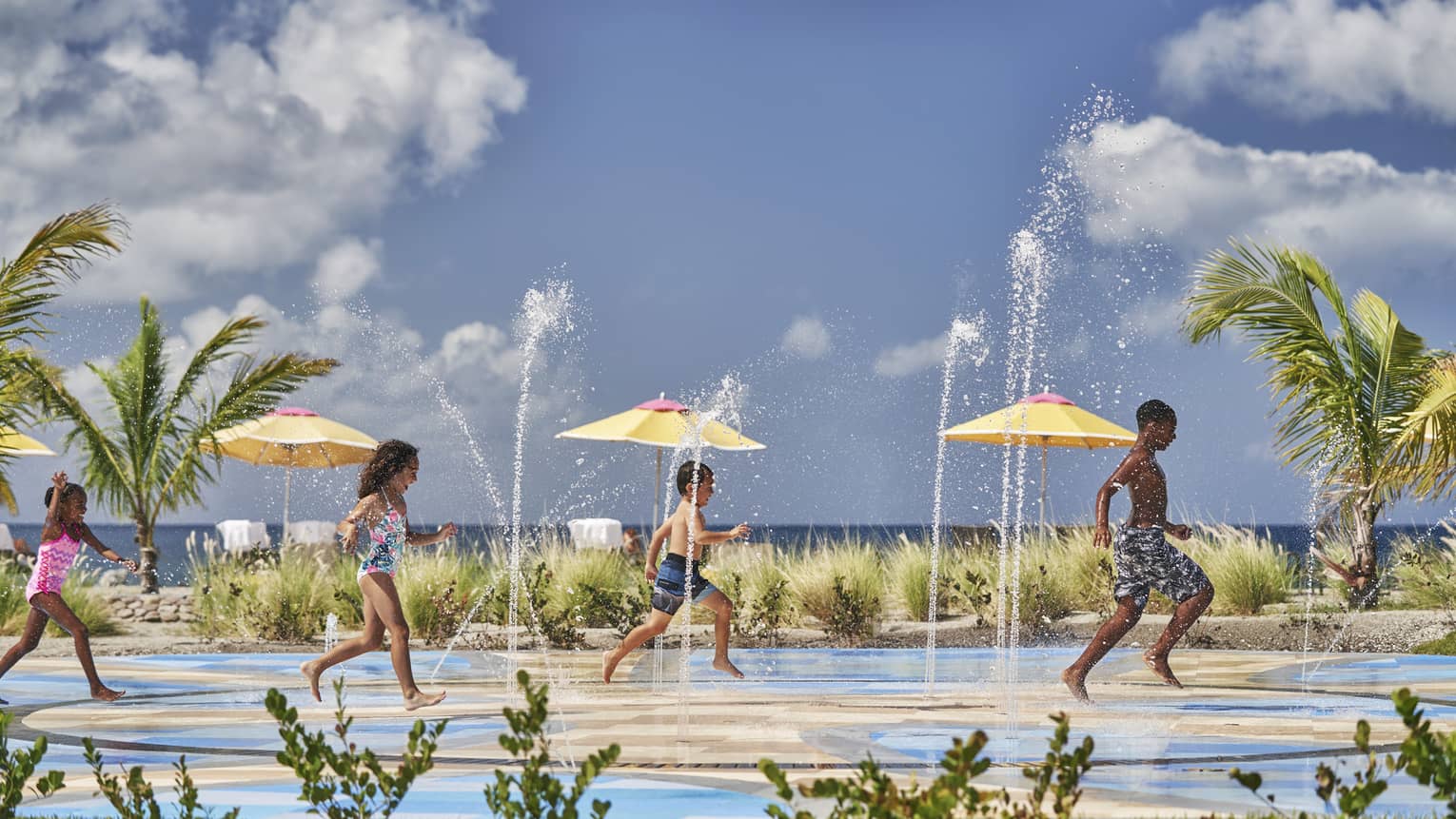 Four kids running and playing on water fountain pad