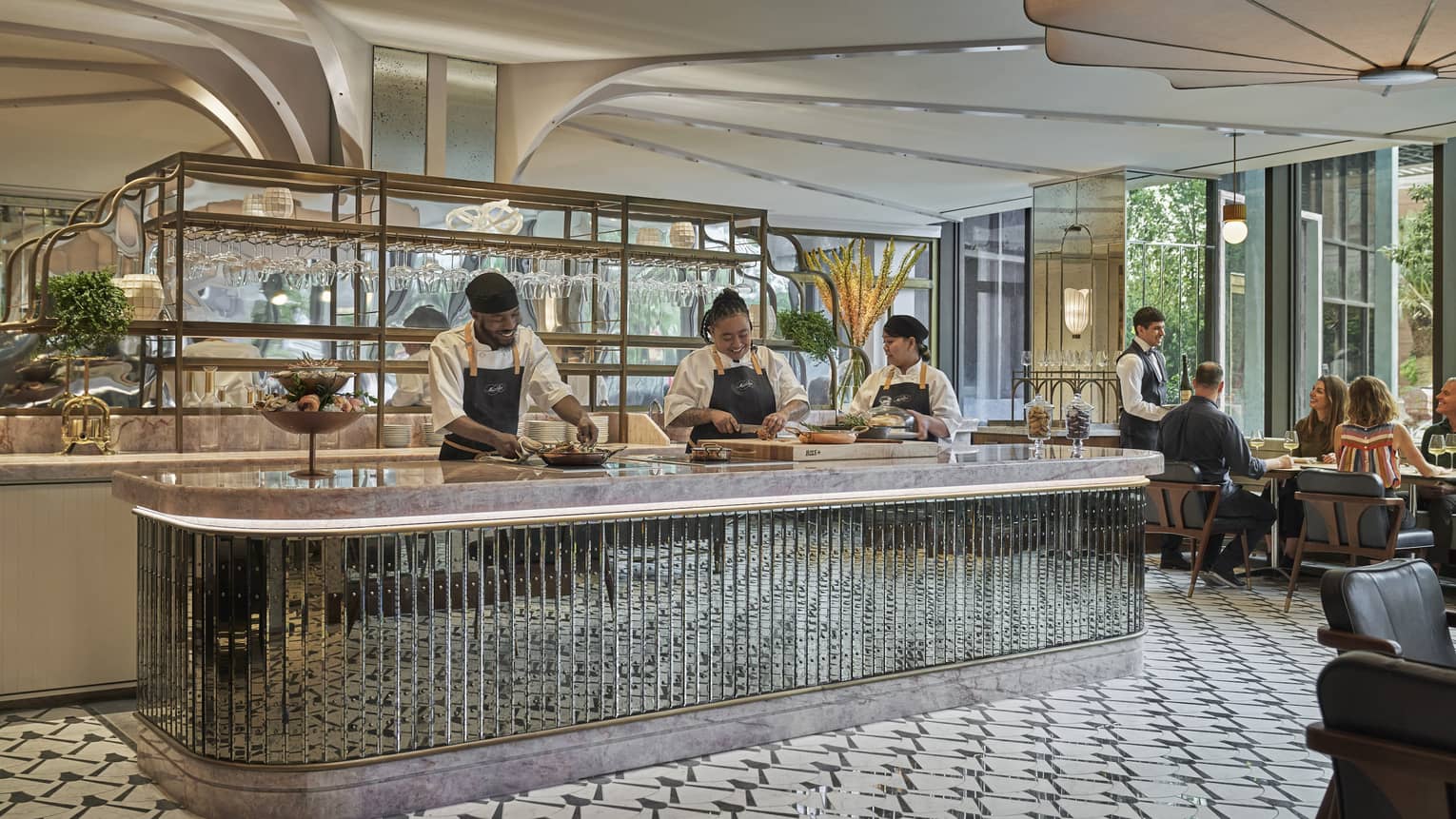 Three staff members prepare dishes behind the counter at Miss River, a table of guests being served in the background