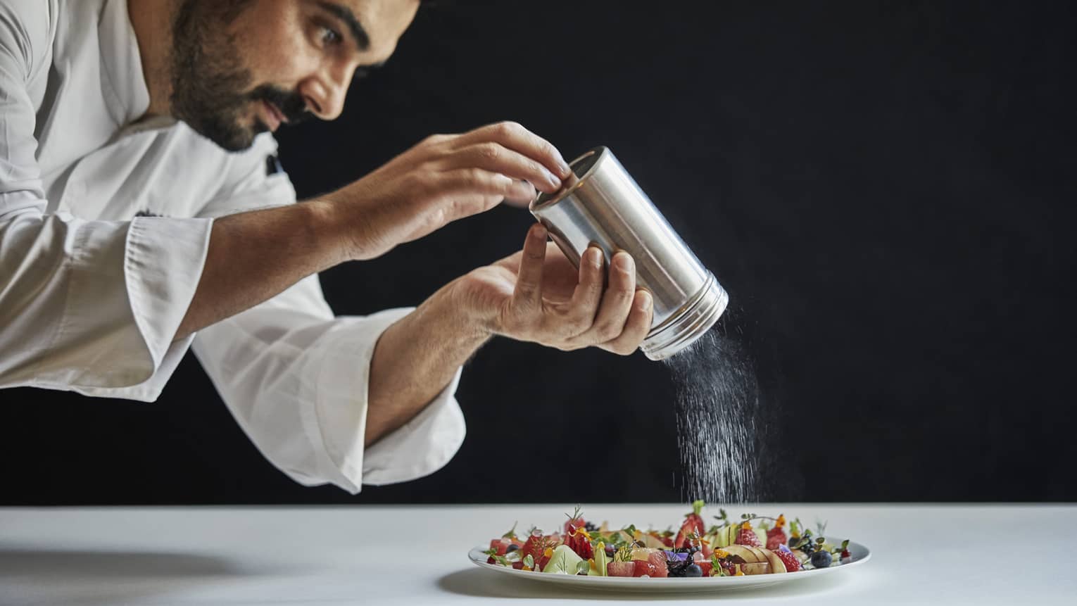 Executive Chef Antonio Mermolia shakes powdered sugar over plate of dessert 