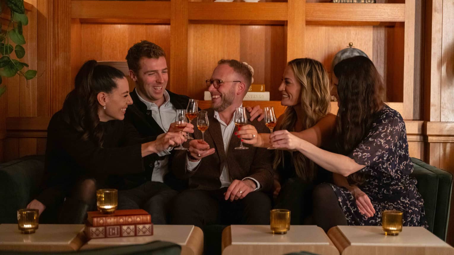 Group of smiling friends on couch raise their glasses in a toast