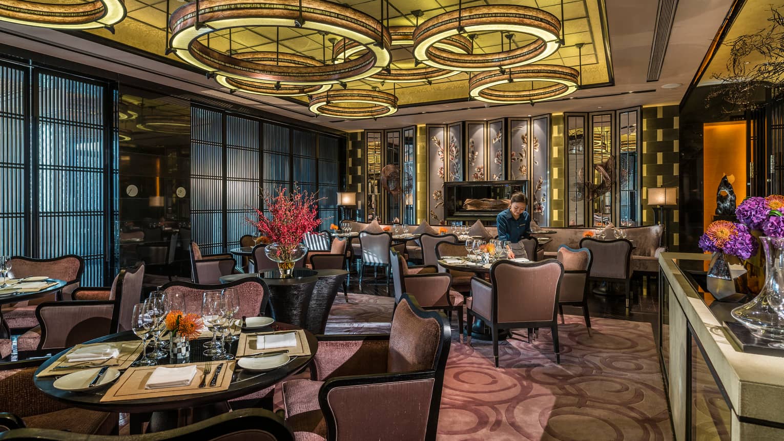 Server sets table in Foo dining room with purple velvet chairs, modern circular lights