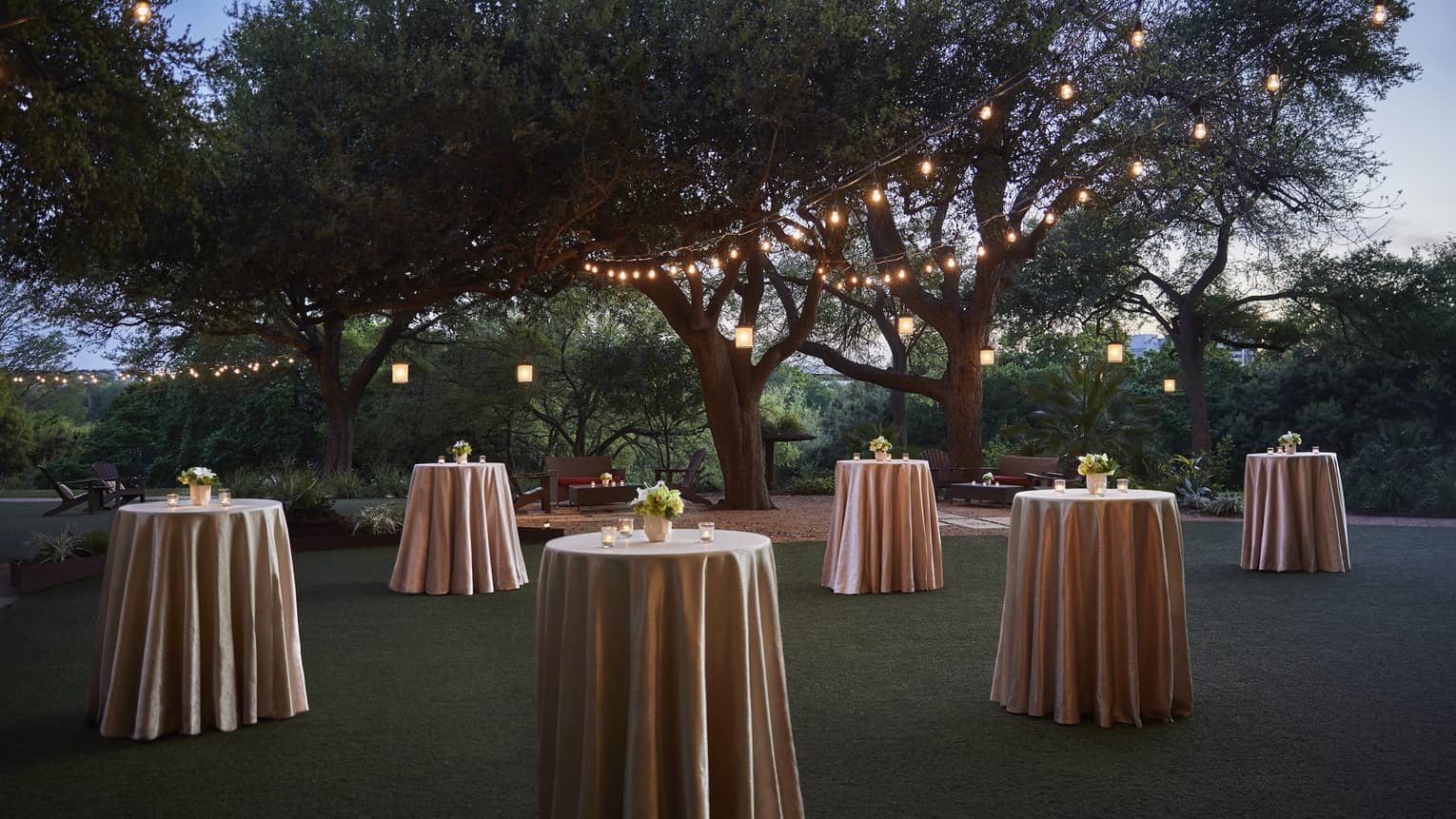 Small cocktail tables with silk linens across event lawn at night