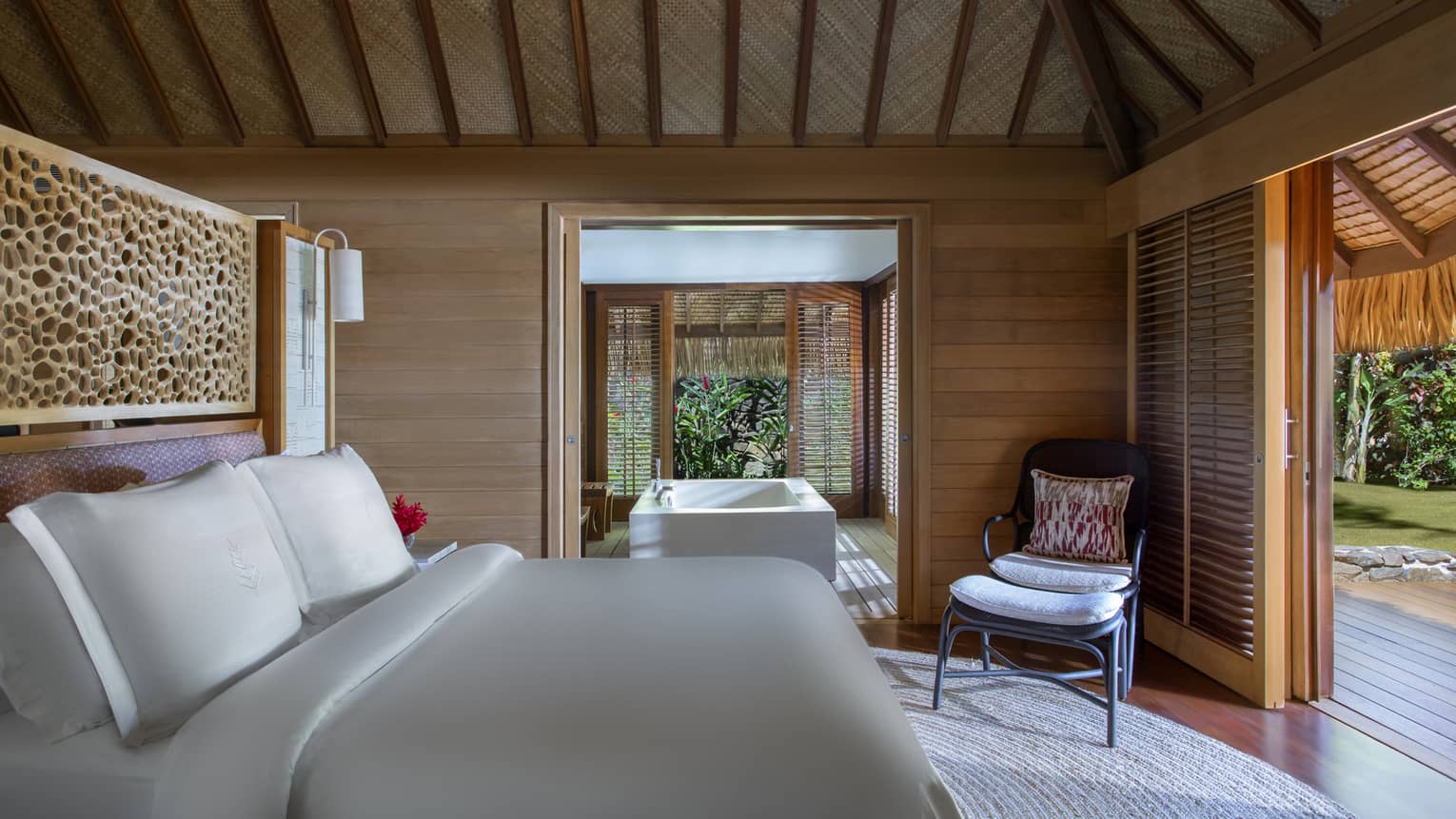 Bungalow villa bedroom with adjoining tub room, bed facing chair, open wall to patio