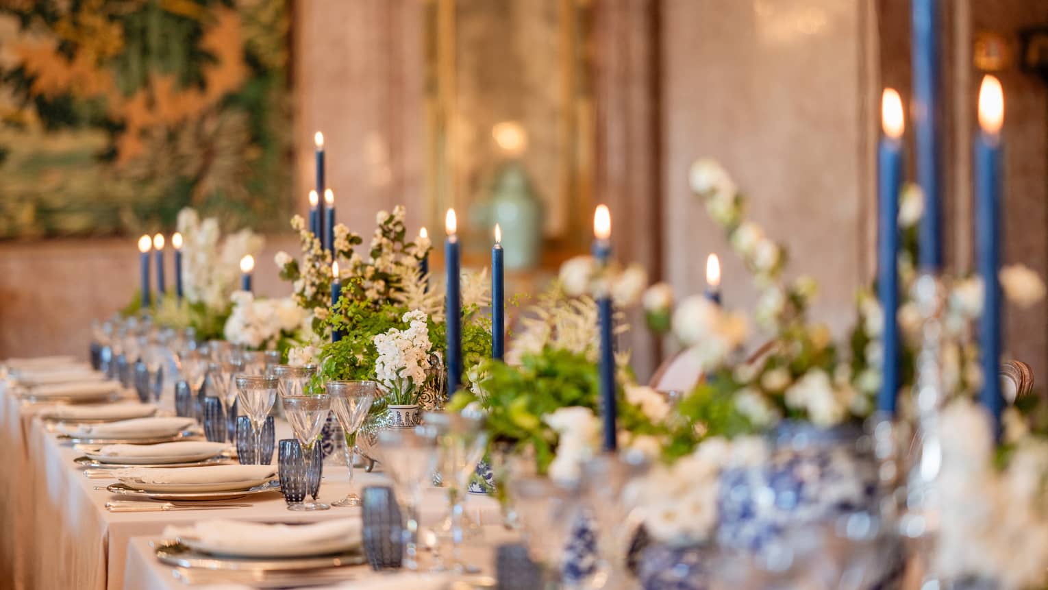 Elegantly set formal banquet table with blue glassware and lit candles interspersed with white flower arrangements