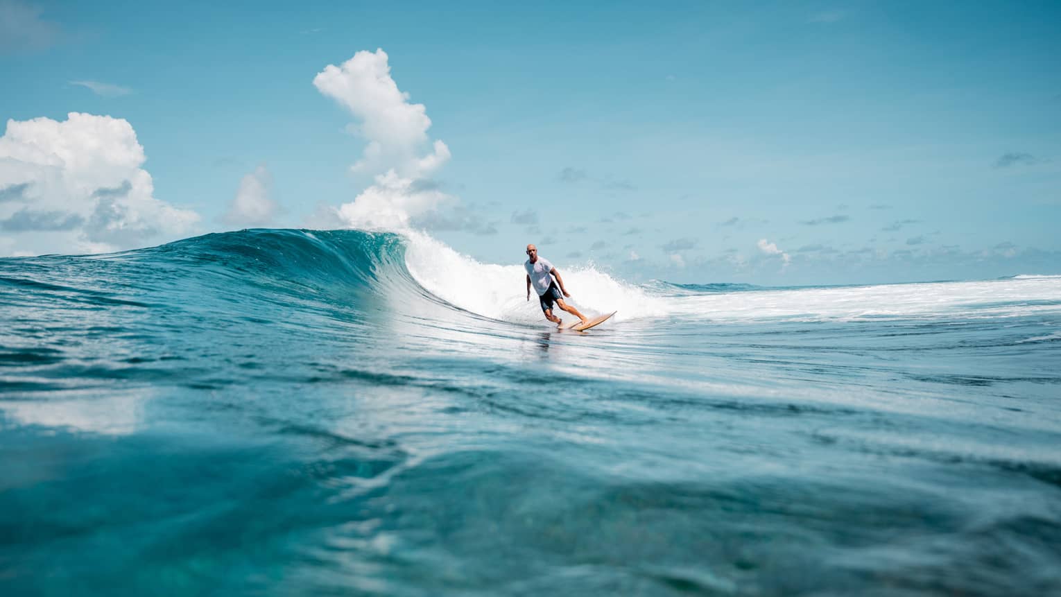 A person surfing a wave in the ocean, the water is a deep blue matched by the blue sky.
