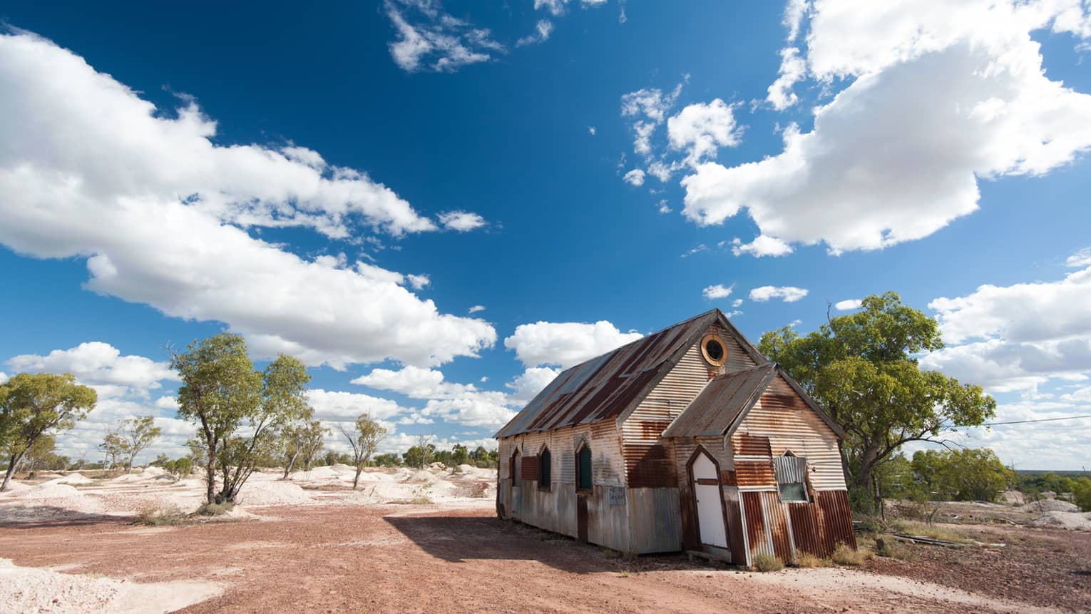 Ramshackle house in Australian outback, sparse trees and blue skies with fluffy clouds