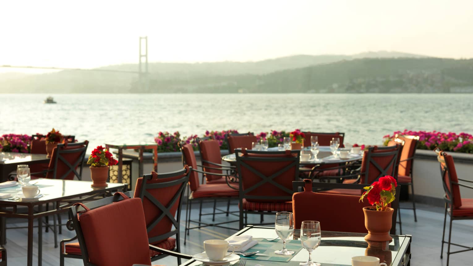 Red dining chairs around Aqua restaurant patio tables by sea 